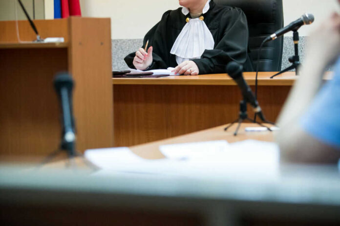 Judge at desk in courtroom with microphones visible