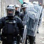Police officers in riot gear down alleyway