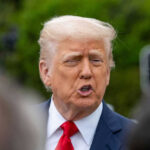 Person in suit talking outdoors with trees background