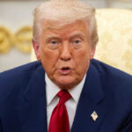 Man in suit with red tie speaking indoors