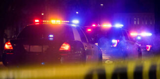 Police cars with flashing lights behind caution tape