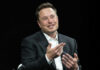 Tesla’s Billionaire Gamble: Will Musk Hit $1 Trillion? Smiling man gesturing while sitting wearing a suit