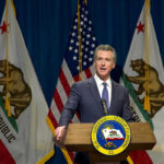 Newsom’s Ex-Chief ARRESTED – Massive Fraud Uncovered Man speaking at podium with California and US flags