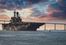 Massive Cover-Up: Navy Hid Deadly Plutonium Aircraft carrier near bridge under colorful sunset sky