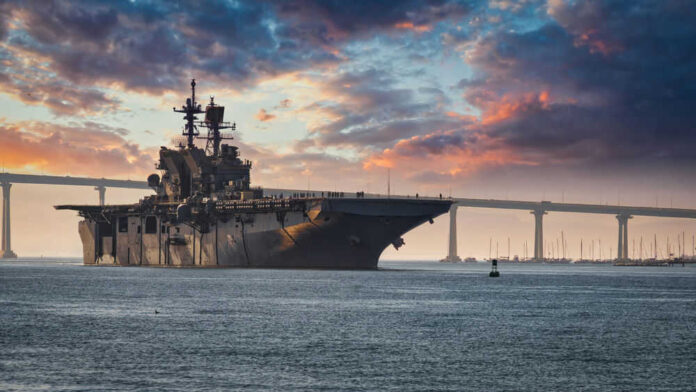 Aircraft carrier near bridge under colorful sunset sky
