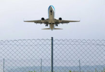 Airplane taking off above a wire fence
