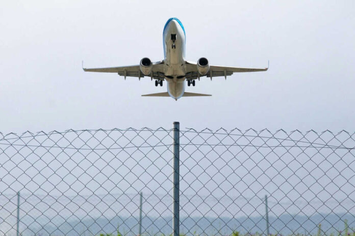 Airplane taking off above a wire fence