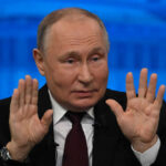 Man in suit raising both hands speaking