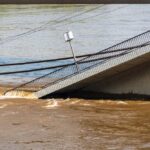A partially collapsed bridge over a brown river due to flooding